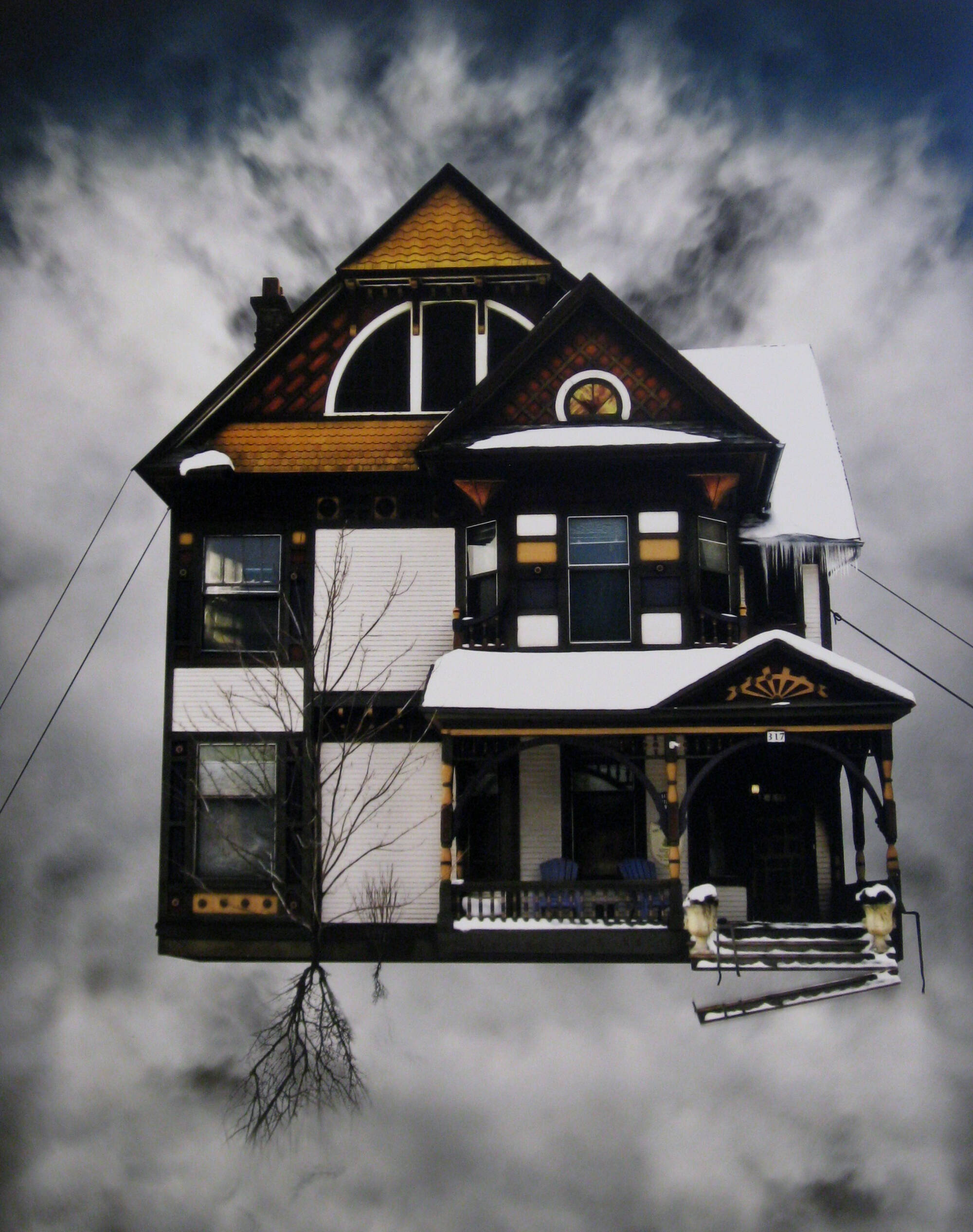 A photograph of a home suspended in thee air. The house is brown with many windows with brightly colored curtains.